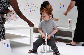 Children playing with colourful dot shaped stickers in a white room.