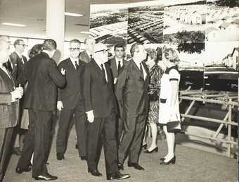 A group of people in front of a photographic artwork, predominantly men in dark suits