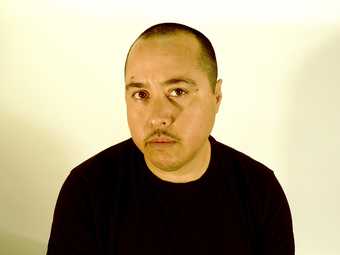 Portrait of Chris E. Vargas in front of a white background, wearing a black shirt. 