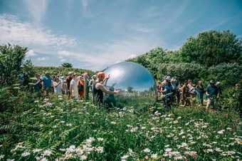 photograph of a large Silver Ball in amongst wildflowers with people stood around 