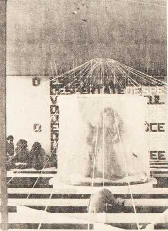 Grainy newsprint image of Anthropomagic Village - an object or figure in a translucent round tent with lines extending outward from the ceiling above, out to a black-and-white striped floor
