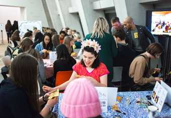 people sit at a table in Tate Modern and embroider on a square of yellow fabric