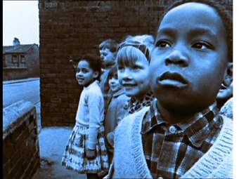 Film still of children standing together on a street looking away or at the camera and smiling