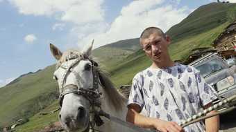 A man is seen with a white horse in a mountain village.