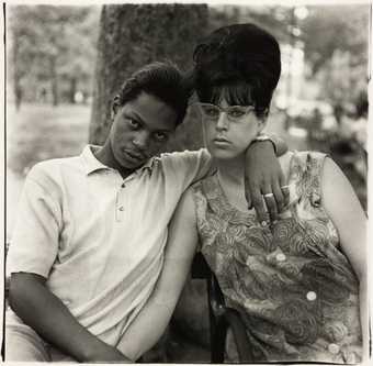 black and white photograph of a man with his arm around a woman, they stare at the camera