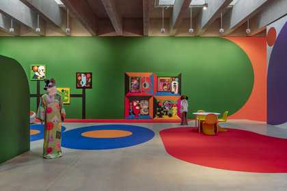 A large room with brightly painted floors and walls. two mannequins with animal heads punctuate the space along with a table a chairs.