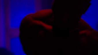 The shadowy head and shoulders of a figure with subtle red and blue lighting in a dimly lit environment