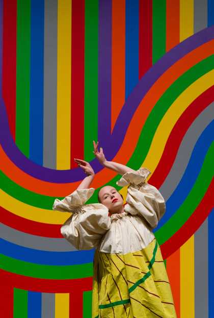 Woman in a bright striped dress in front of a matching background.