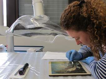 a person uses a cotton swap to carefully remove varnish from a landscape painting