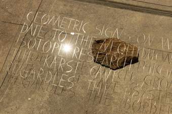 A clear sheet with letters inscribed above a stone floor and a single rock.