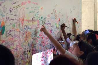 A group of young people drawing and writing with colourful markers onto a white wall.