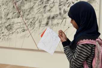 A young person drawing into a small sketchbook in the galleries.