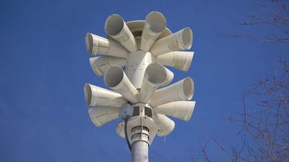 A large white speaker device against a bright blue sky