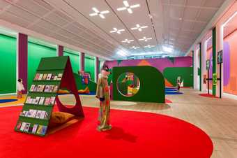 an install photograph of figures with animal heads in a colourful gallery space, a zine magazine rack appears in front