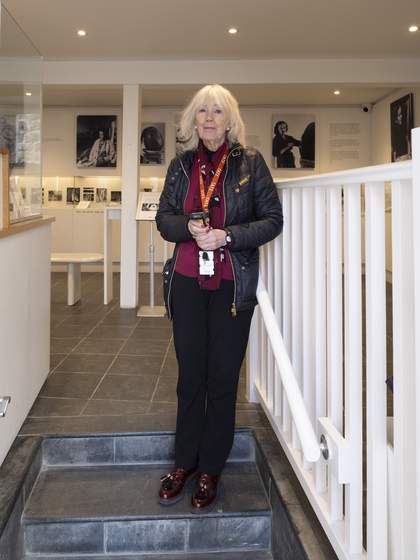 A Visitor Assistant wearing an orange Tate lanyard standing on a stone step inside the entrance of the museum.