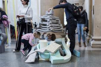 A family plays with foam bricks and flat forms to create a tower and play underneath it