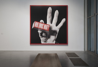 a photomontage artwork of a black and white hand holding a red and white piece of text that says 'who owns what?'