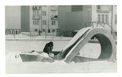 A black-and-white image of a circular sculpture in the snow with a woman observing its detail.