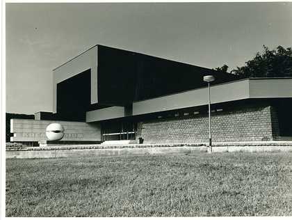 A black-and-white photo of a white, circular sculpture outside a crematorium. .