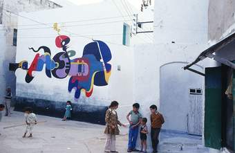 A photograph of a abstract mural by M. Labied taken outside with children in the foreground