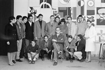 A black-and-white photograph of a group of fifteen people posing for the camera in front of a backdrop of multiple abstract artworks