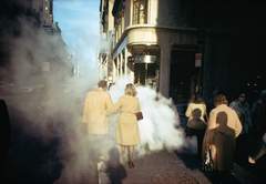Man and woman walking away along a city road through smoke.
