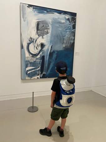 Child wearing a Tate St Ives explorer backpack standing in front of a painting, looking at the artwork