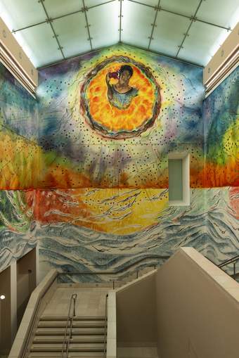 A large wall above a staircase painted with a colourful mural featuring a dark skinned figure