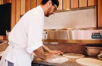 A chef in a kitchen rolling out pizza dough