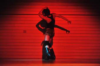 A person dancing against a red wall wearing cowboy boots