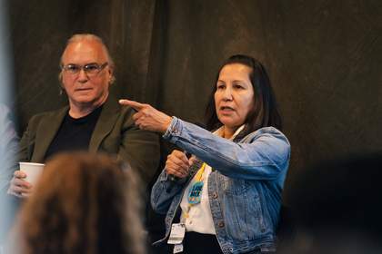 A photograph depicting a man and a woman, the latter of which is speaking and pointing to something outside of the image frame.