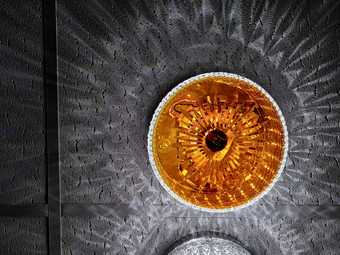 A circular glass ceiling lamp seen from below, with a warm glow and light patterns radiating from it