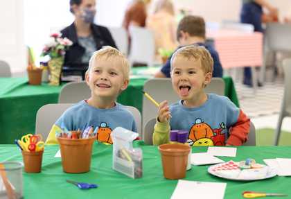 Two children sat at a table laughing and sticking their tongue out