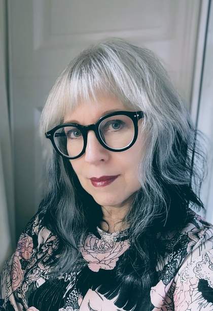 Headshot of Amy Hale wearing round black glasses and a black and pink floral top against a neutral background