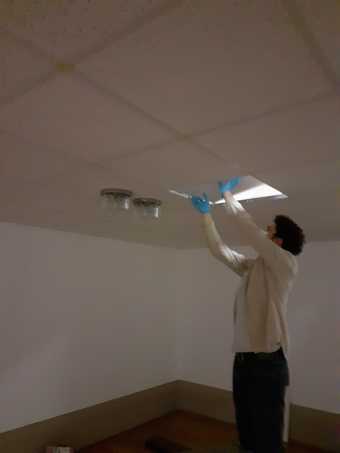 An individual with gloved hands putting a ceiling tile in place