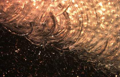 A photomicrograph showing where the brush dragged still-wet black paint from the hair into an area of lighter paint, and detail of the figure’s dark hair with a glossy sheen