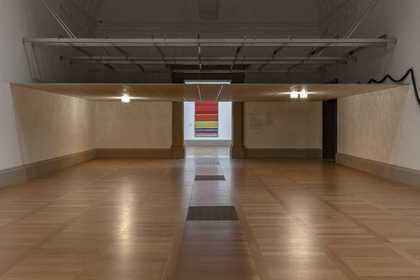 A room in an art gallery with a low ceiling made of tiles, with lamps attached that emit warm lighting