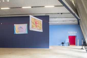 Brightly coloured pieces of material featuring images of bodily organs and written text hang high up in a gallery space, while next to them is an archway with ‘Lubaina Himid’ written above it in large letters