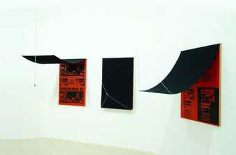 Three rectangles on a gallery wall, all with red backgrounds with black text and silkscreened images, including of police violence against students. They each have a black cover that can be lifted using a string mechanism. Two are shown revealed here.