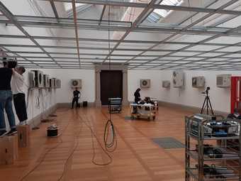 Several individuals in an art gallery arranging lengths of wire that connect wall-mounted ceiling fans together
