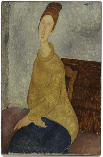 Three-quarter portrait of Hébuterne, seated with hands crossed in her lap. Her red hair is piled up high. Dark yellow rollneck sweater and dark blue skirt. She sits in a wooden chair. Behind is a square of brown, perhaps the back of a painting.