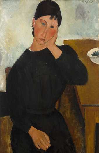 Woman with short dark hair and simple, long-sleeved black dress sits with her arm resting on a table, her face resting in her hand. Her facial features are pronounced, elongated, with flushed cheeks and dark grey hollows for eyes. Narrow portrait format.