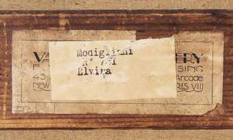 A label stuck on top of another label, stuck to wood. Both labels are stained and peeling, the words faded or large sections covered up. The clearest words appear on the uppermost label: ‘Modigliani’ and ‘Elvira’.