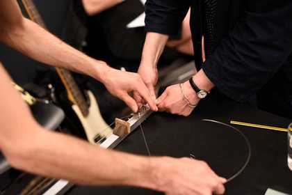 Two people replace the strings on a guitar-like instrument