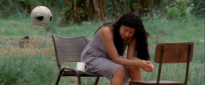 Woman sat on a chair, in the grass, with another chair facing her, there is a white mug next to her.