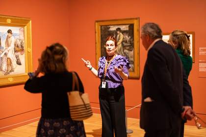 A person talking to two people about a painting in a gallery