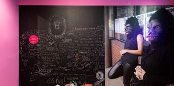 a chalk board with writing on it with the Guerrilla Girls in gorilla masks standing by it