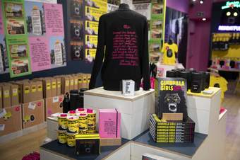 a table with shop products by the Guerrilla Girls on it including ' dearest art collector' sweatshirt, book, water bottle and mugs