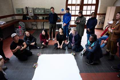 A group of people standing and kneeling in front of a piece of paper on the floor.