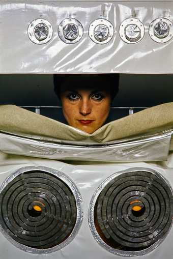 A woman dressed in a PVC costume of a kitchen appliance (an oven).